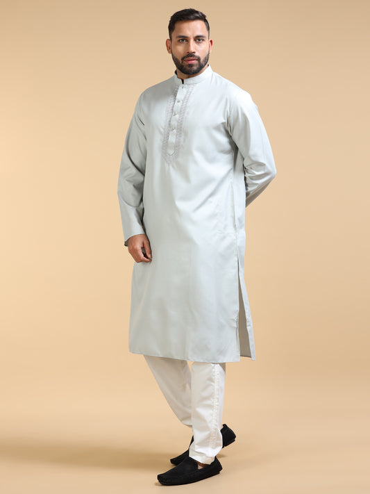 Man wearing a light gray kurta with white pants on a beige background