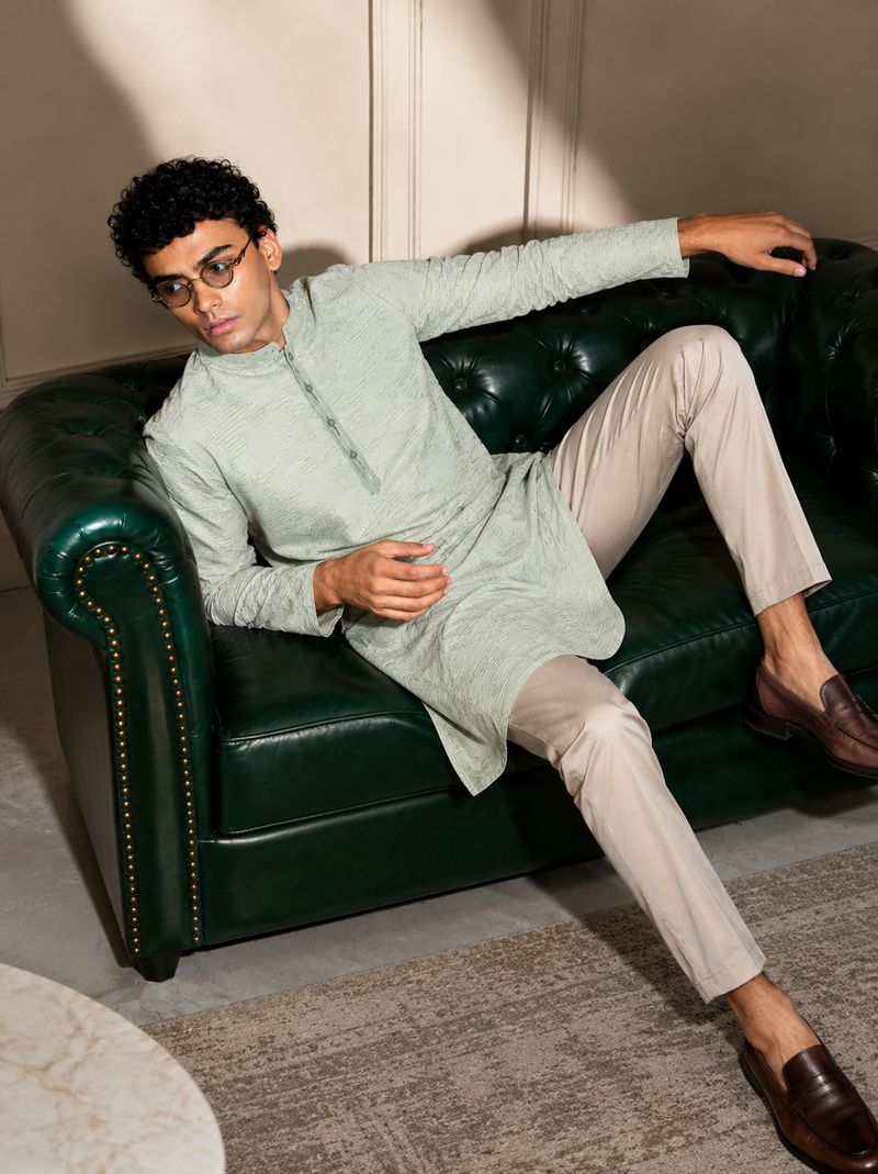 Man in a sage green kurta reclining on a green leather sofa