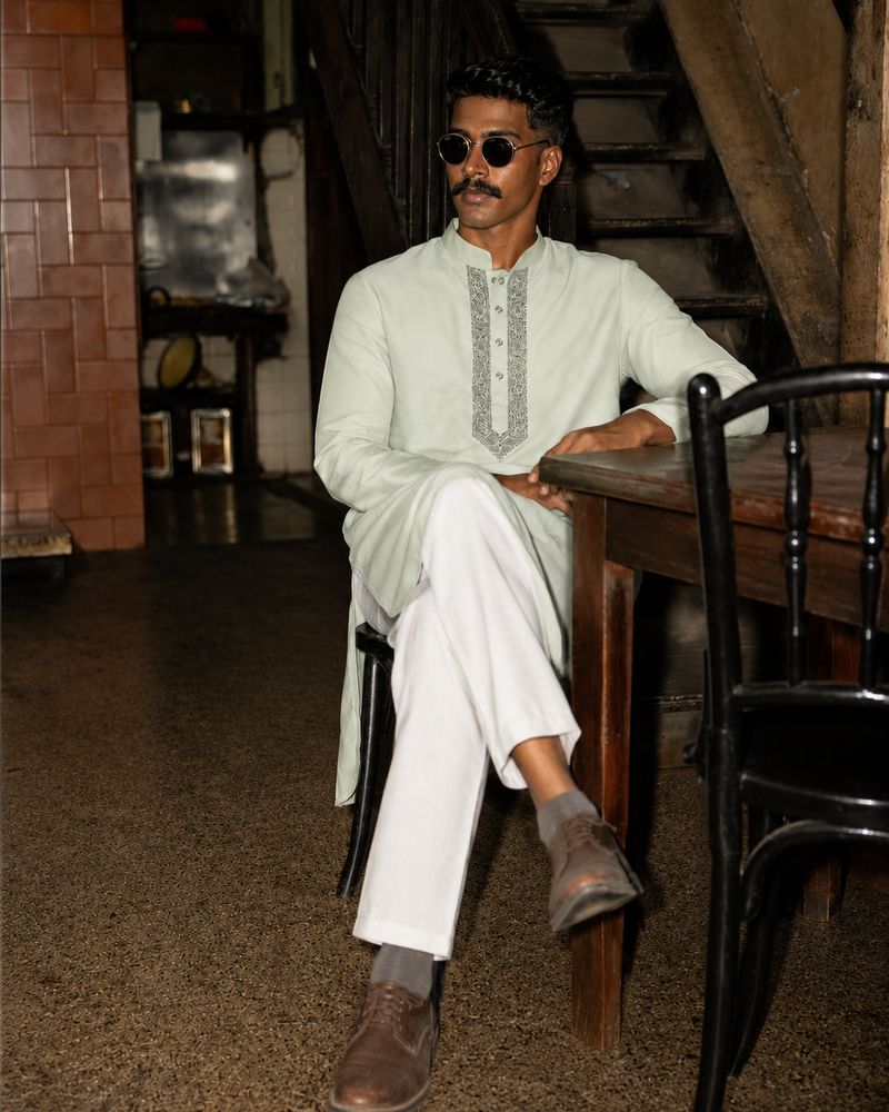 Man in a mint green kurta seated at a wooden table