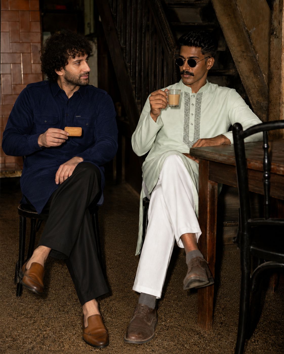 Two men in a kurta and shirt sharing tea in a vintage café